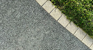 a tarmac driveway separated from grass with a brick border