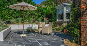 a brick patio with a rattan table and chairs and a parasol in the back garden of a brick house