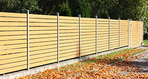 a newly installed wooden fence to a property with fallen leaves on the ground below