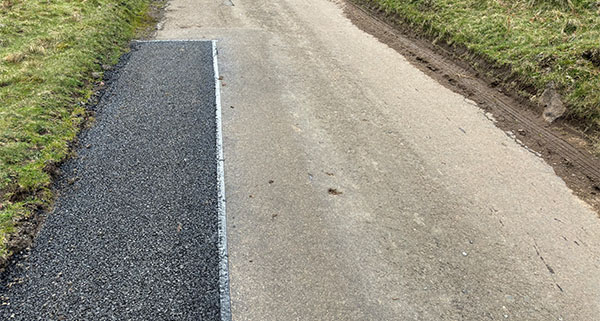 a rural road with a tarmac patch to fill in a pothole on the side of a road