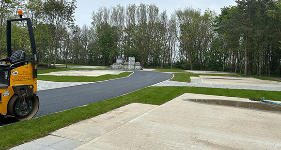 a drum roller sitting on a newly tarmacked road, next to lots ready for construction