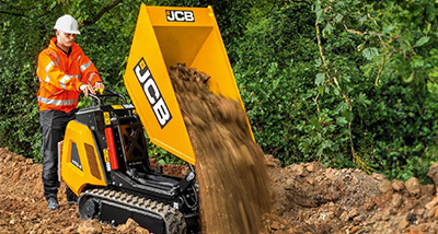 a man in an orange hi-vis jacket and white helmet tipping dirt onto the ground using a yellow tracked dumper